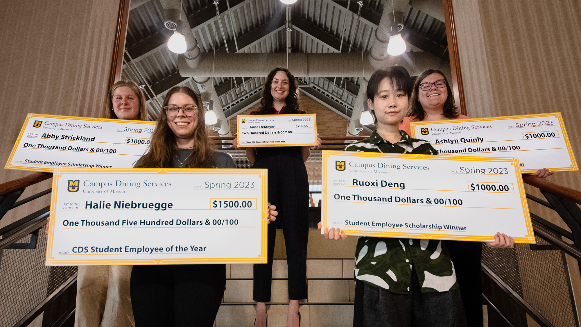 Five scholarship-recipient students hold oversized checks on stairs